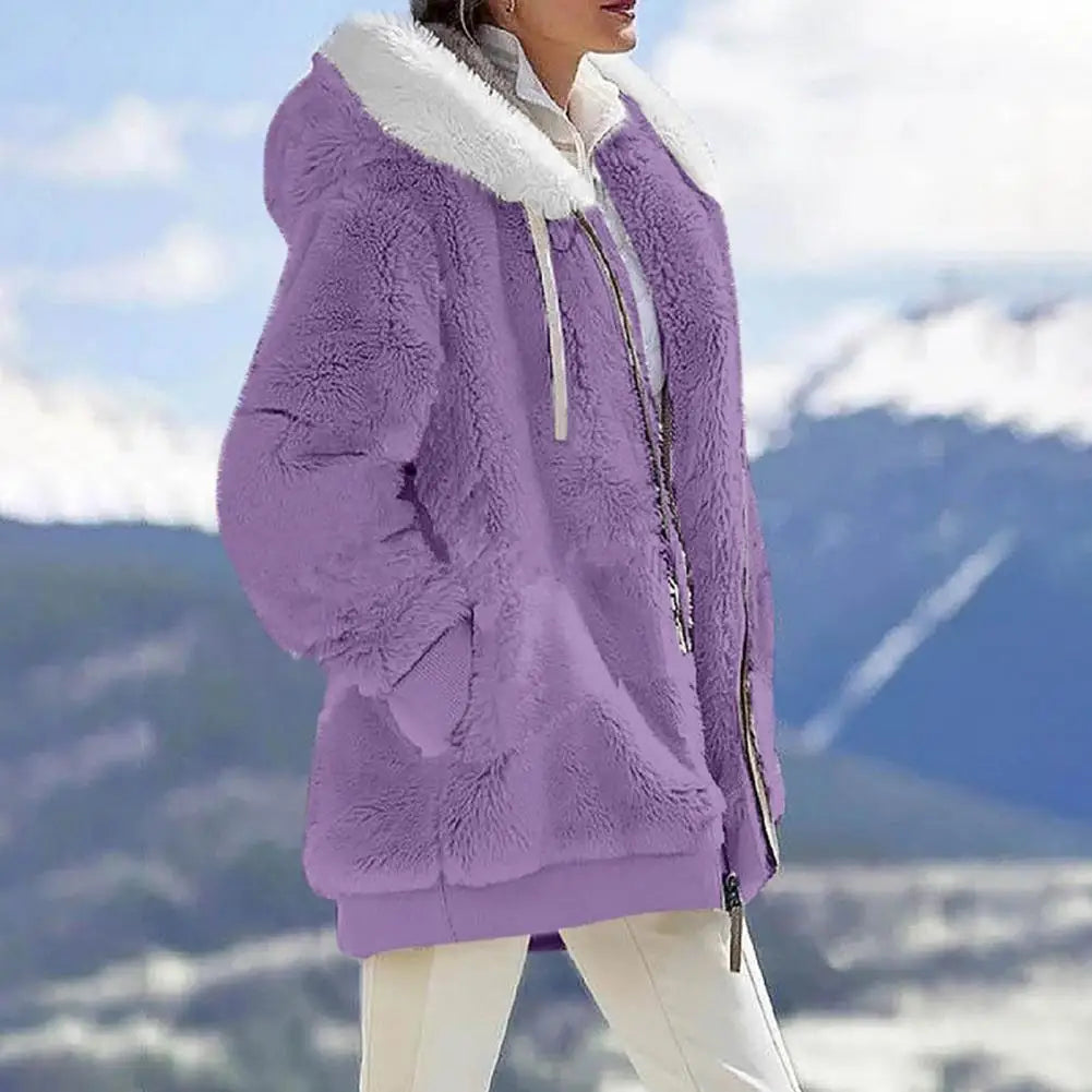 Woman wearing a loose plush hooded jacket in purple with a soft collar against a scenic mountain background.